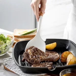 Cream white silicone spatula with short wooden handle flipping steak in a grill pan