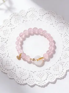 Close-up of a natural rose quartz bracelet with a white agate donut charm and gold details.