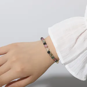 Close-up of a colorful tourmaline beaded bracelet on a woman's wrist with white sleeve.