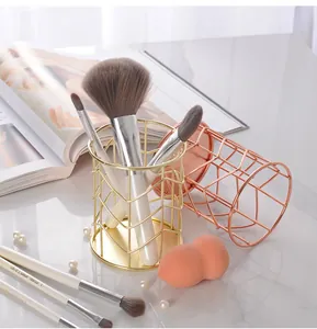 Detailed view of golden iron wire mesh makeup brush holder on marble desk with pearls