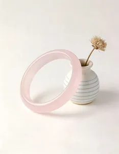 Close-up of translucent pink crystal bangle resting against a small ceramic vase.