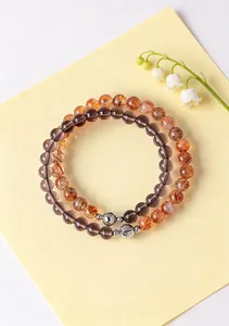 Natural smoky crystal and orange sunstone beaded bracelets on yellow paper with lily flowers.