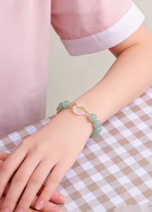 Elegant green beaded bracelet featuring white agate ring and gold luck charm on a wrist.