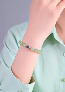 Detailed view of natural green crystal beaded bracelet with silver charm on wrist