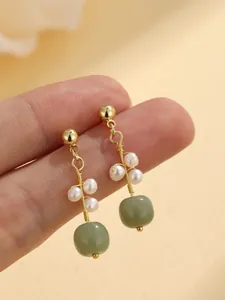 Close-up detail of elegant gold earrings featuring white pearls and round green jade beads