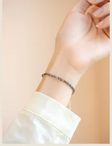 Close-up of 2mm silver obsidian beaded bracelet on female wrist with white shirt sleeve.