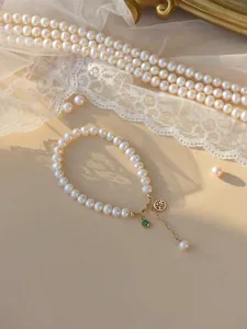 Close-up of elegant freshwater pearl bracelet with golden lucky charm and green gem