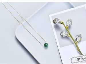 Detailed view of a delicate gold chain necklace featuring a round green gemstone pendant