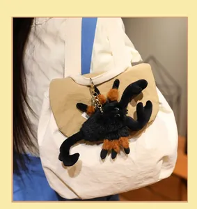 Close-up view of a realistic black scorpion plush keychain hanging on a beige canvas bag