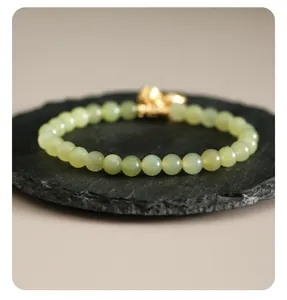 Detailaufnahme eines Armbands aus grüner Hetian-Jade mit goldenem Lotus-Anhänger