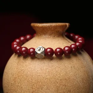 Handmade red cinnabar bead bracelet with a silver lucky charm displayed on a vintage ceramic jar