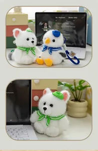 Detailed view of a cute plush polar fox keychain in a green sailor outfit on a desk.