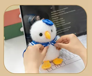 Close-up of a cute white seagull plush keychain charm being adjusted by hands on a laptop