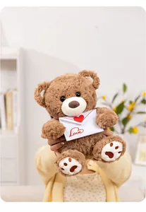 Nahaufnahme eines braunen Teddybären mit einem weißen 'Love'-Umschlag als Geschenk zum Valentinstag