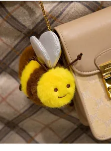 Gros plan d'un mignon porte-clés abeille en peluche jaune sur un sac à main beige.