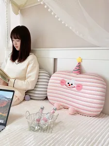 Close-up of a pink striped cartoon nap pillow placed on a bed in a cozy bedroom scene
