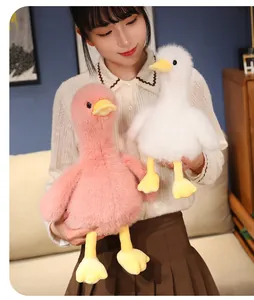 Soft plush duck toys in pink and white held by a person in a cozy indoor setting.