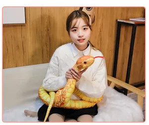 Long realistic yellow python plush toy held by an Asian model in cozy home decor setting.