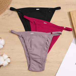 Set van drie katoenen bikini-slips met dunne bandjes en metalen ringen op houten achtergrond.
