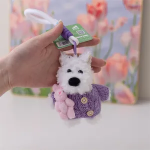 Dettaglio di un portachiavi in peluche Westie bianco con maglione lavorato a maglia viola.