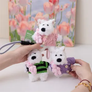 Dettaglio di tre portachiavi in peluche West Highland Terrier bianchi con maglioni lavorati