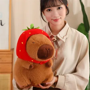 Gros plan d'une peluche capybara avec capuche fraise rouge tenue par une jeune fille