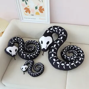 Three sizes of black and white skull patterned snake plush toys displayed on a beige sofa