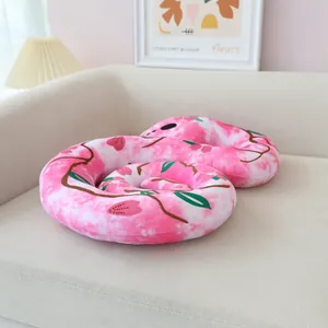 Coiled pink floral snake plush toy resting on a warm cream colored sofa detail view