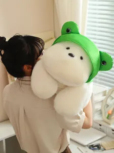 Close-up of a large white plush Westie dog wearing a green frog hat in a cozy room