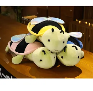 Dettaglio di peluche ibridi tartaruga-ape con ali iridescenti su un tavolo di legno.