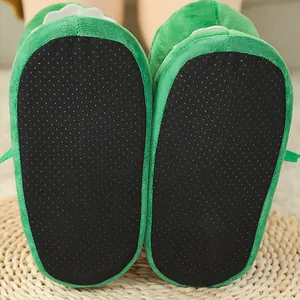 Detailopname van de zwarte antislip-noppenzolen van groene pluche krokodillenpantoffels.