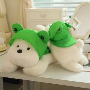 Adorable white plush dog wearing a green frog hat lying on a desk for home decoration
