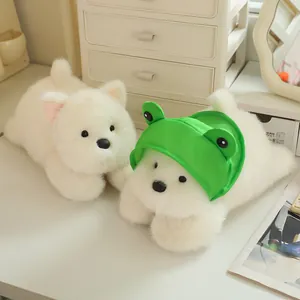 Pair of cute white Westie plush dog dolls, one wearing a green frog hat on a desk.