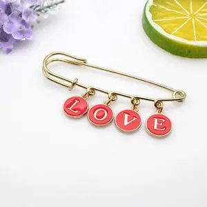 Vista detallada de un broche de imperdible dorado con dijes de esmalte rojo con letras LOVE
