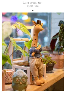 Cute stuffed giraffe doll wearing striped shirt and burlap overalls in a garden setting