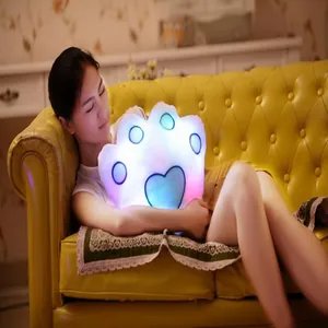 Coussin en peluche lumineux en forme de patte tenu par une fille sur un canapé jaune.
