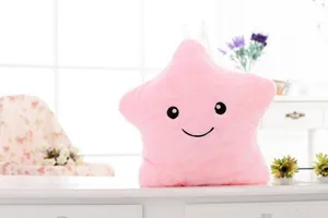 Coussin en peluche doux en forme d'étoile rose avec un joli visage souriant brodé sur table