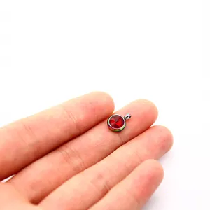 Close-up view of a 10mm rainbow stainless steel red birthstone pendant on fingertips.