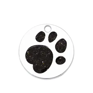Close-up of circular metal pet ID tag with black glitter paw print design on white background.