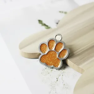 Detailopname van een oranje glinsterende hondenpenning in de vorm van een pootafdruk.