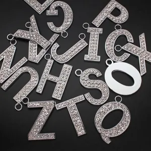 Close-up detail of glittering rhinestone 35mm alphabet pendants on black background.