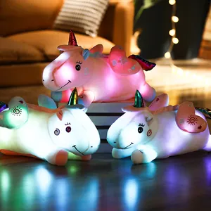 Three glowing LED unicorn plush pillow toys displayed in a warm home bedroom setting