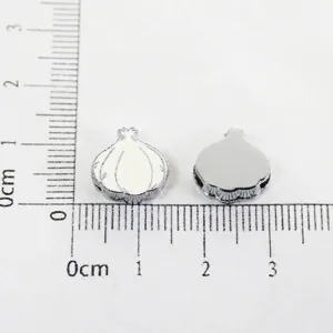 Detailed view of two garlic-shaped alloy beads measured on a centimeter ruler for scale