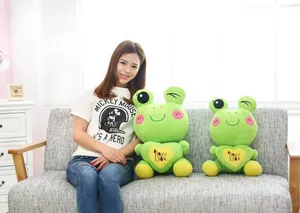 Cute green frog plush toys shown with a model on a comfortable grey sofa.