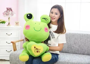Detailed view of a large green frog plush toy with a heart, held by a model in a home.