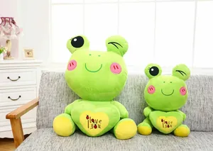 Detailed view of two green plush frog dolls with heart embroidery on a gray sofa