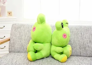 Two cute green cartoon frog plush toys sitting back-to-back on a cozy grey sofa