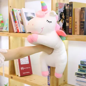 Soft white plush unicorn with rainbow horn and wings being hugged on a shelf