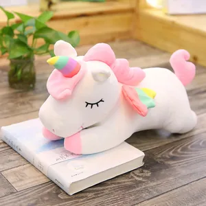 Cute soft white unicorn plush toy with rainbow horn and wings resting on a book