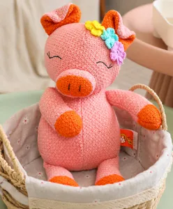 Détail d'une peluche de cochon rose tricotée avec des fleurs dans un panier tressé.